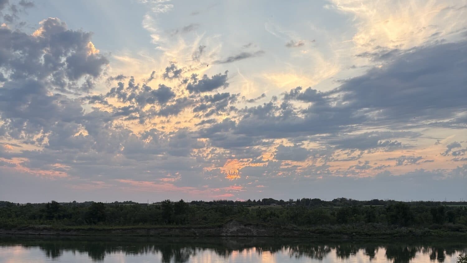 Sunset over a prairie river in Saskatchewan, clouds mirrored in the still water.