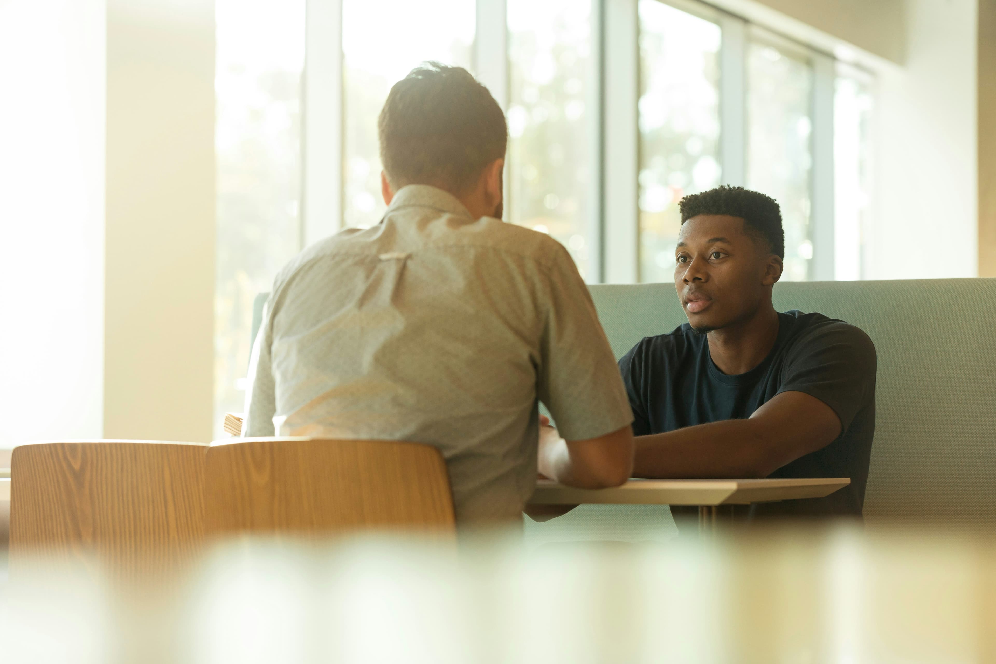 A man in conversation with a clinician across a table in a bright clinic setting